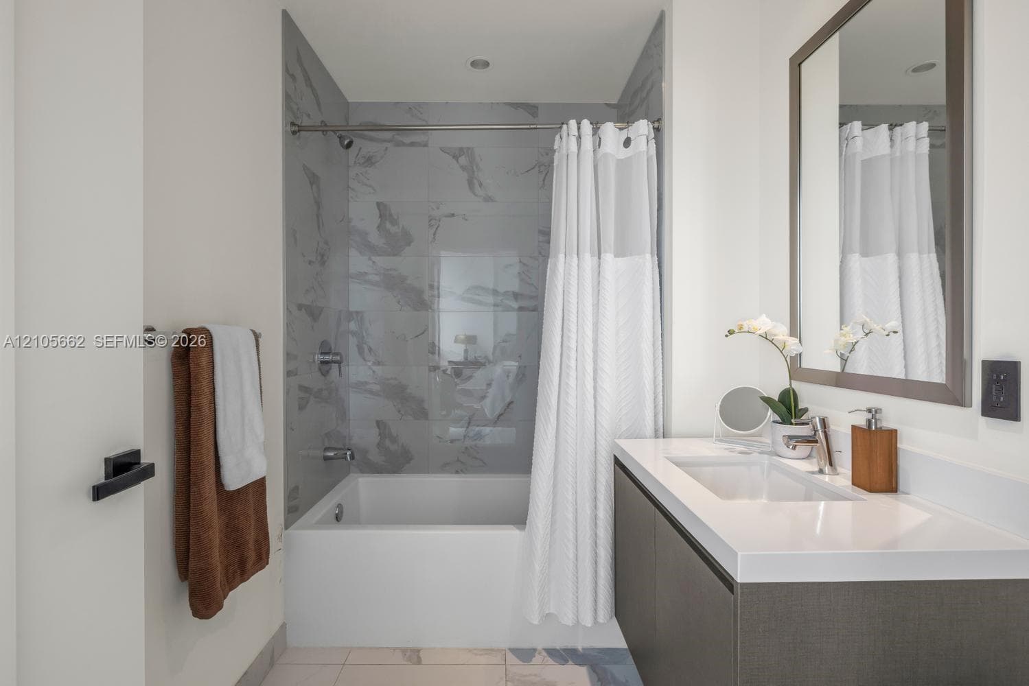 Wall-mounted floating vanity with integrated rectangular sink and solid surface countertop, mirror with framed border, and bathtub featuring patterned wall tile