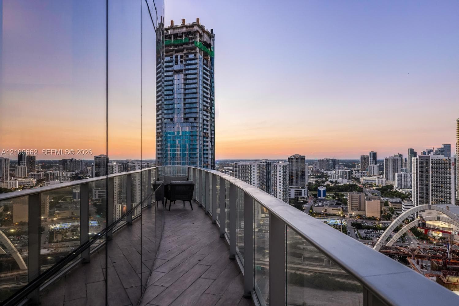 Curved balcony featuring wood-finish flooring, glass panel railings, and full-height exterior glass facade