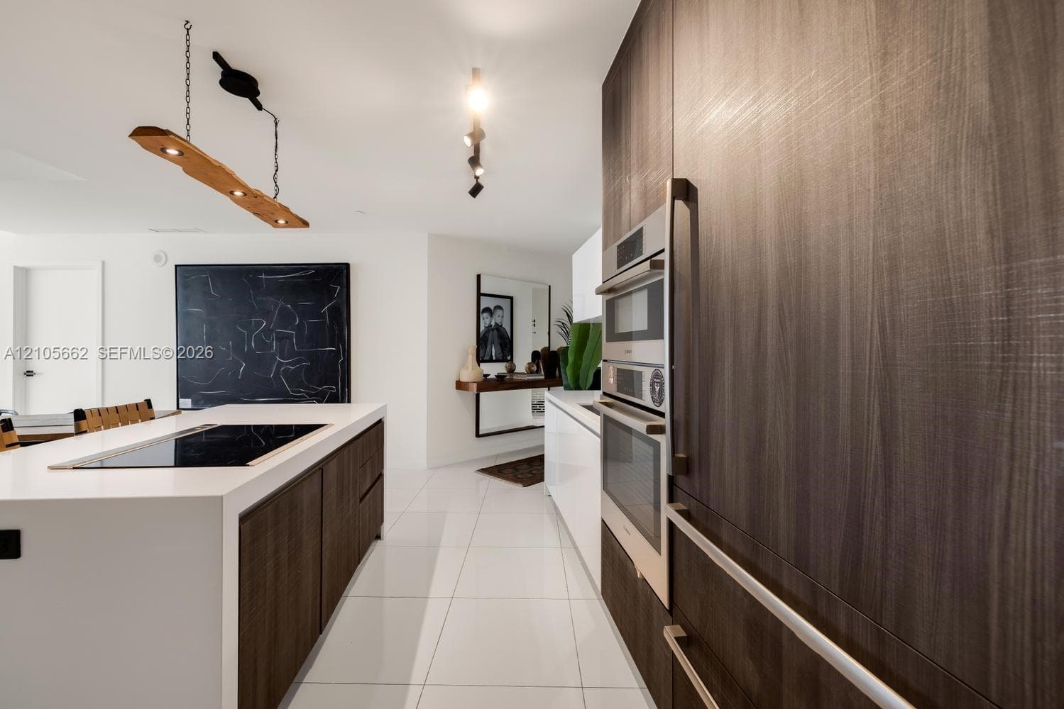 Kitchen featuring full-height wood-finish cabinetry, built-in double wall ovens, a large island with a surface-integrated cooktop, and large-format porcelain tile flooring