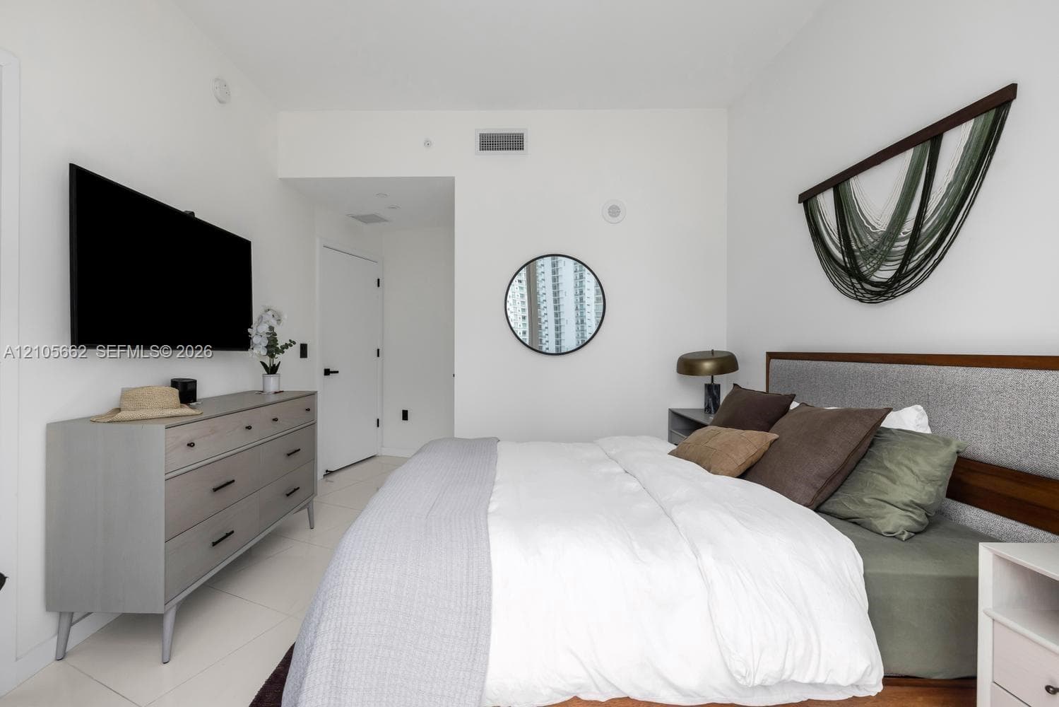 Neutral-toned room featuring large-format tile flooring, smooth white wall finishes, and a circular wall-mounted mirror