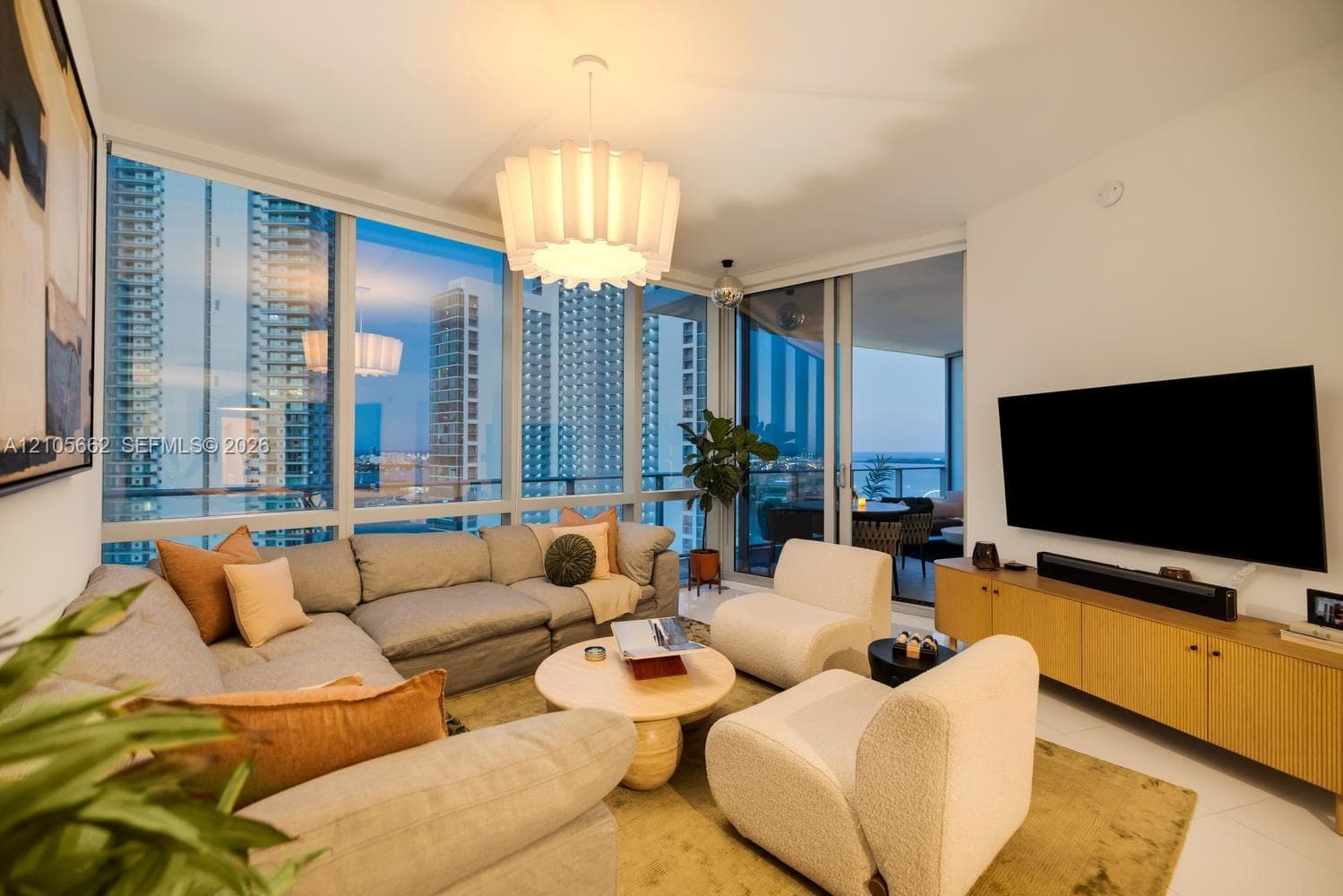 Living area featuring floor-to-ceiling windows, white tile flooring, custom drum pendant lighting, and a sliding glass door providing external access