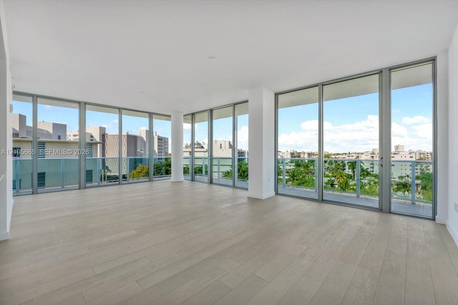 Floor-to-ceiling windows, wood-finish flooring, and an expansive balcony with glass railings