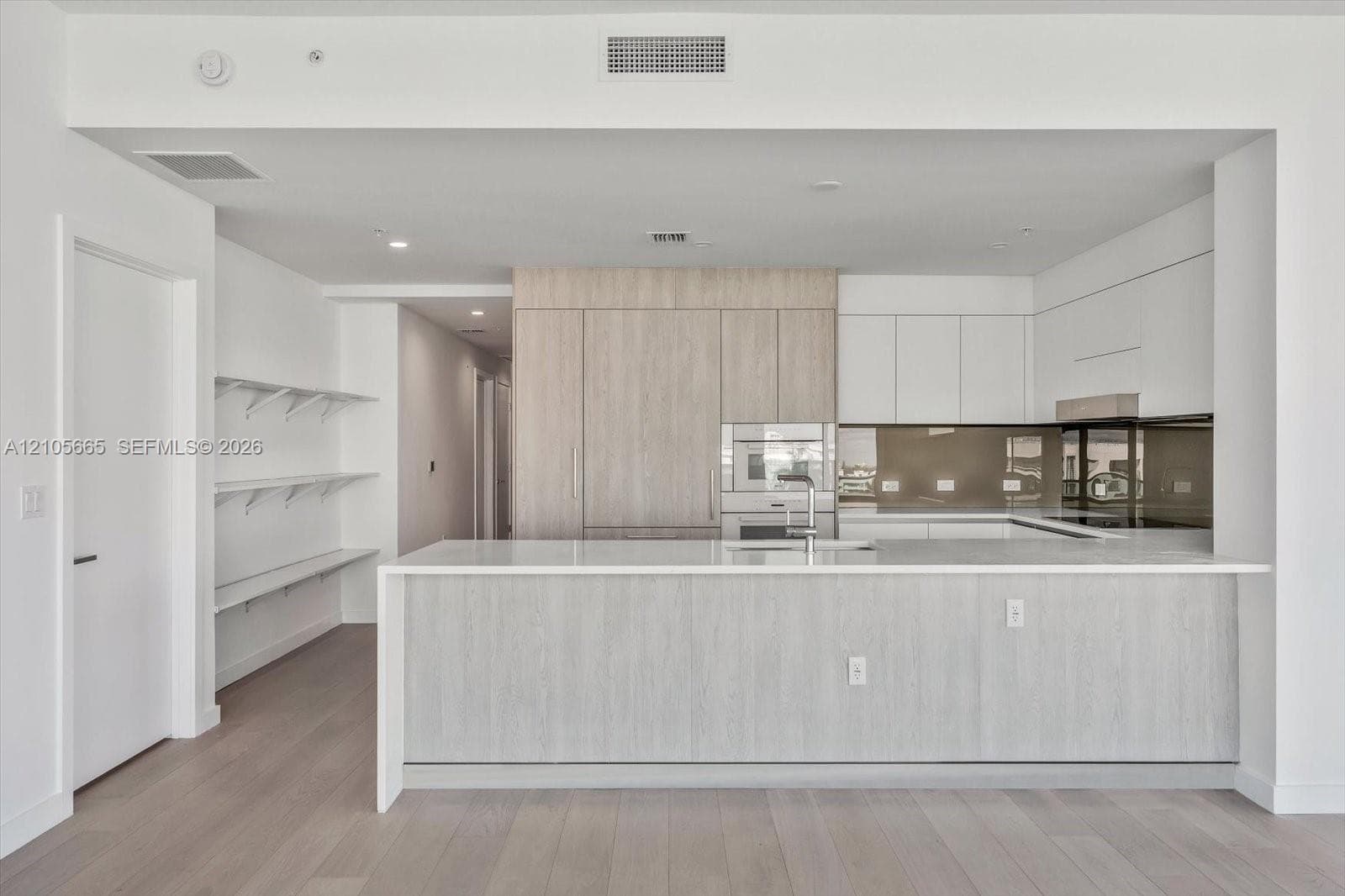 Kitchen featuring a waterfall-edge quartz countertop, two-tone cabinetry with wood-finish and flat-panel white finishes, integrated appliances, and a reflective glass backsplash