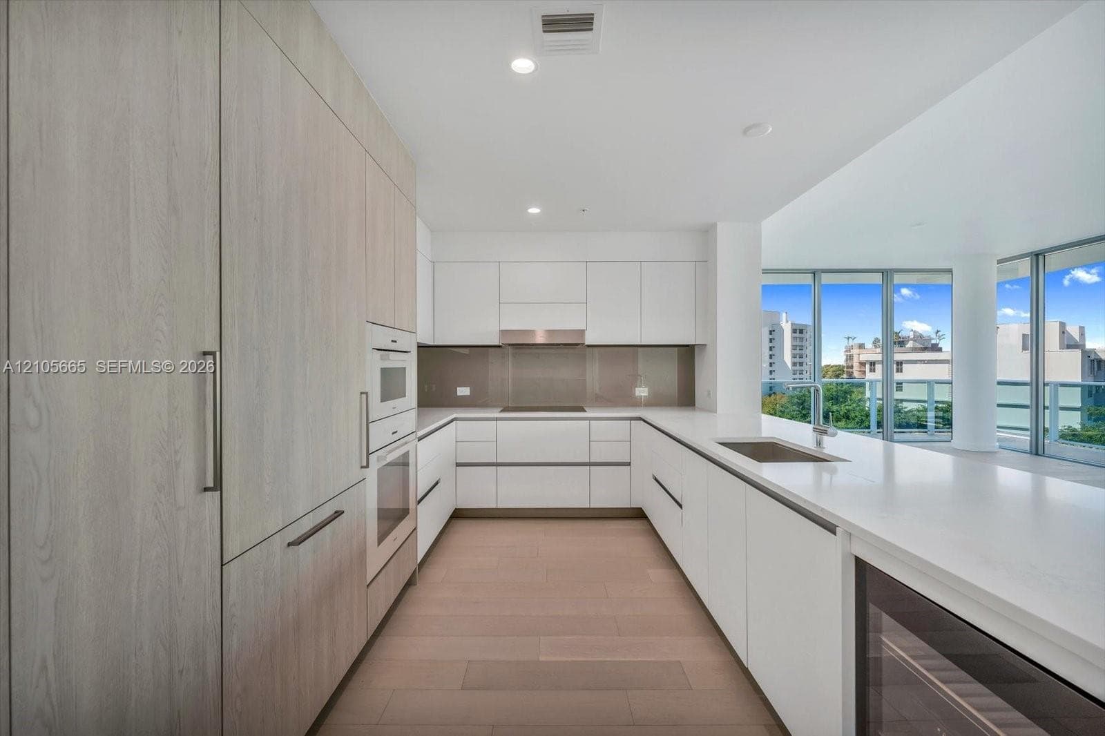 Kitchen featuring flat-panel cabinetry, quartz countertops, integrated stainless steel appliances, a glass backsplash, and wood-finish flooring
