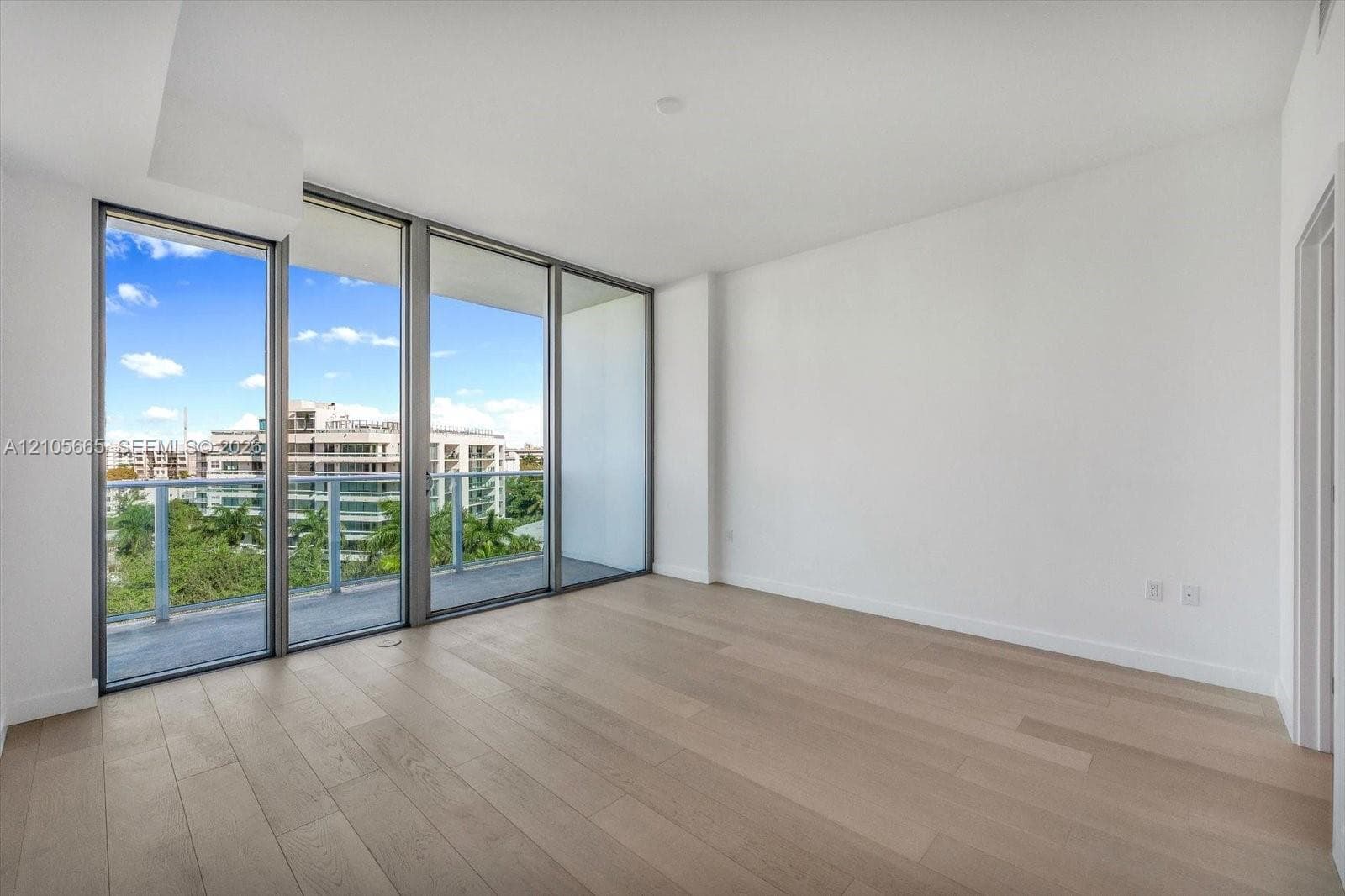 Floor-to-ceiling windows, wood-finish flooring, and a glass-railed balcony with exterior urban scenery