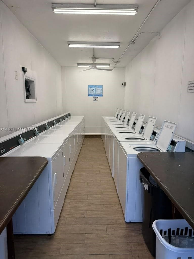 Laundry facility equipped with multiple top-loading washing machines, wood-finish flooring, and built-in folding counters