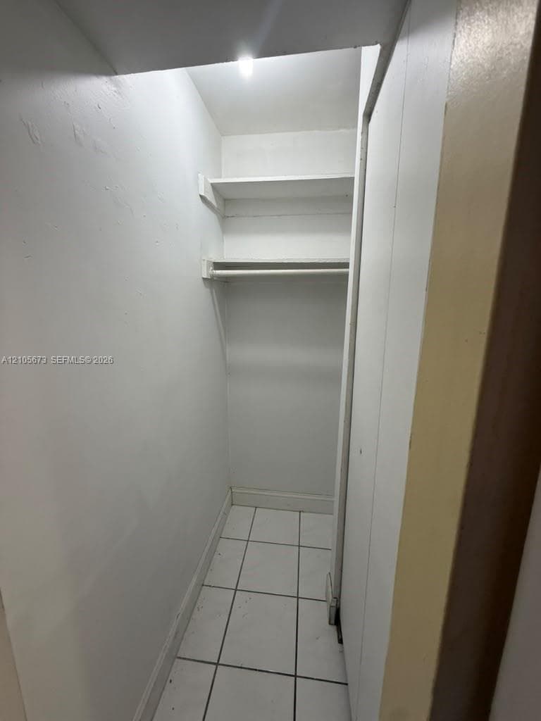 Reach-in closet featuring white ceramic tile flooring, built-in shelving, and a garment rod