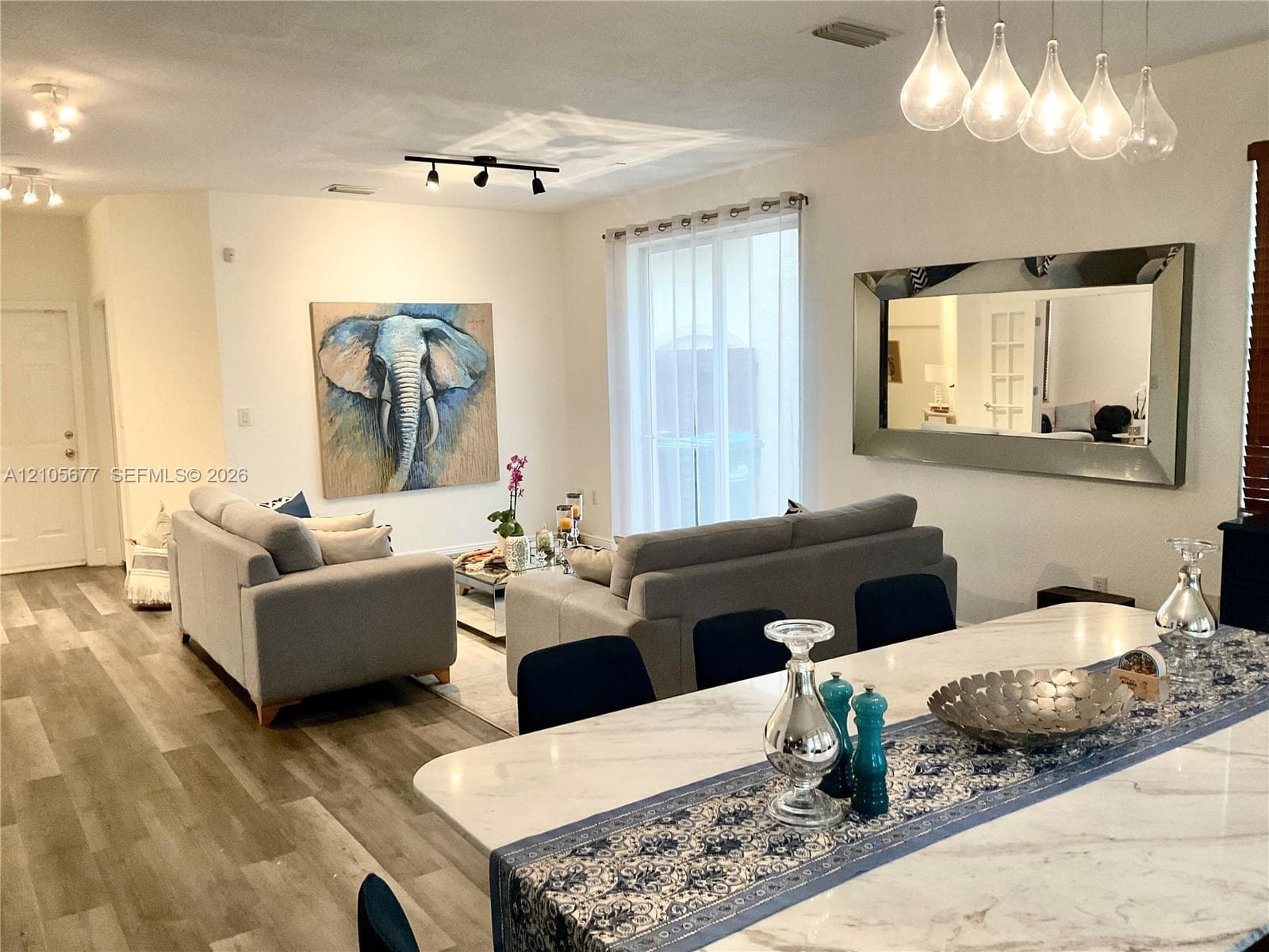 Open-concept interior featuring wood-finish flooring, multi-pendant lighting, track lighting, sliding glass door, and a stone-surface kitchen island
