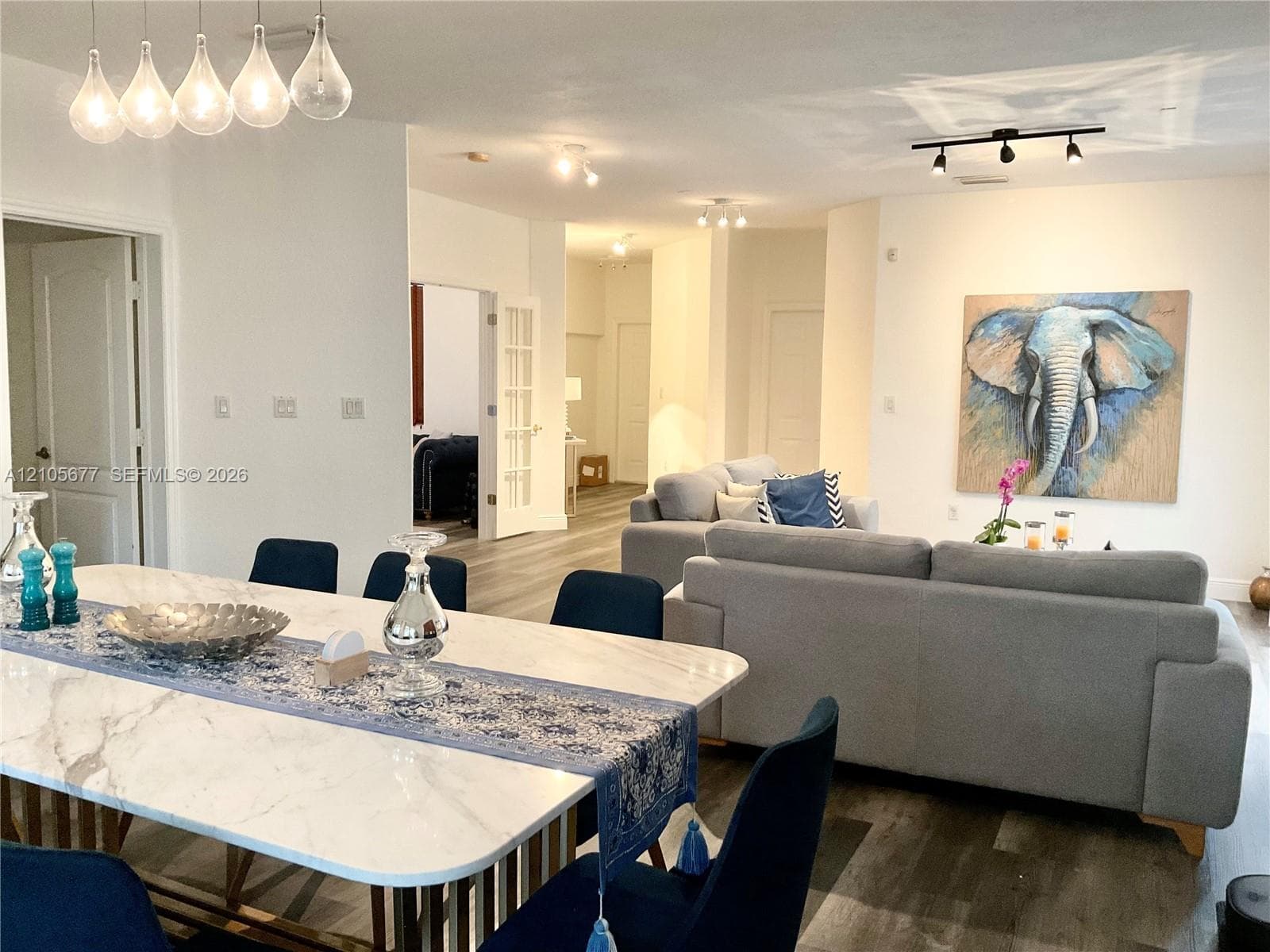 Open-concept interior featuring wood-finish flooring, a contemporary five-pendant linear light fixture, recessed track lighting, and a set of French doors