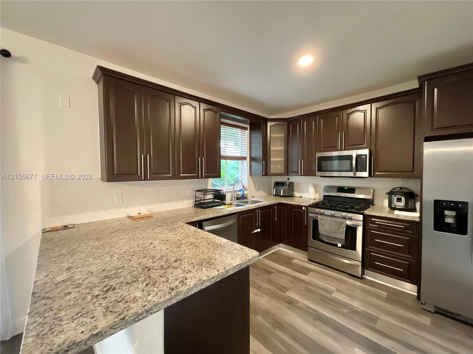 Kitchen featuring dark wood cabinetry, stone-finish countertops, stainless steel appliances, white subway tile backsplash, and wood-finish flooring