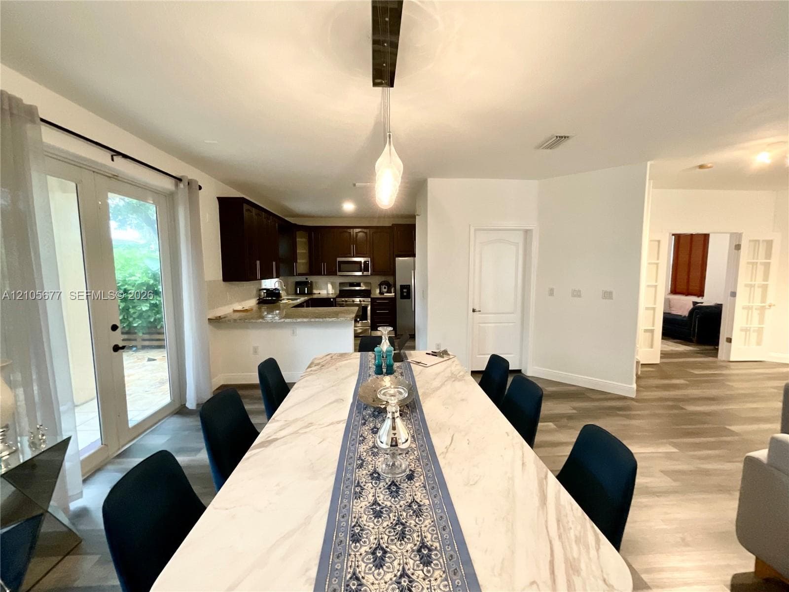 Kitchen featuring dark-toned cabinetry, light-toned stone-surface countertops, and stainless steel appliances, with wood-finish flooring and glass-paneled french doors