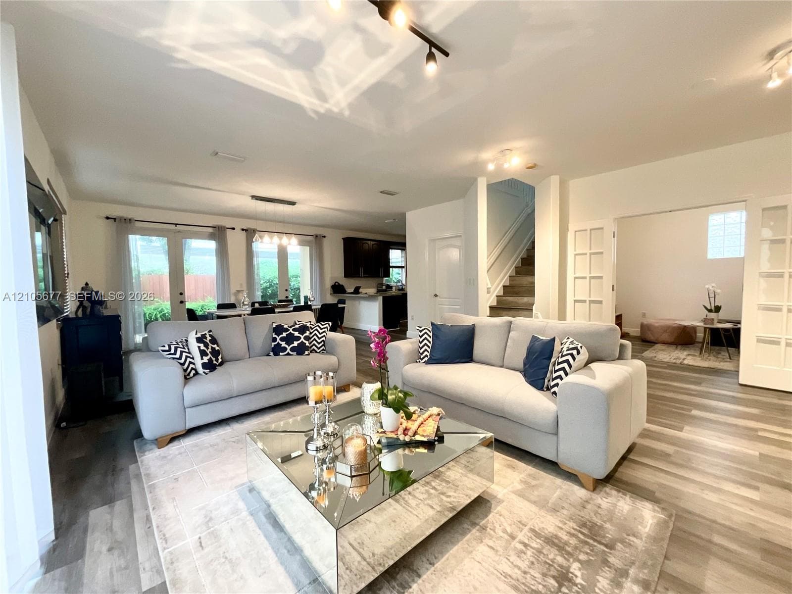 Open interior space featuring wood-finish flooring, recessed track lighting, glass-paneled doors, and a staircase with a white railing