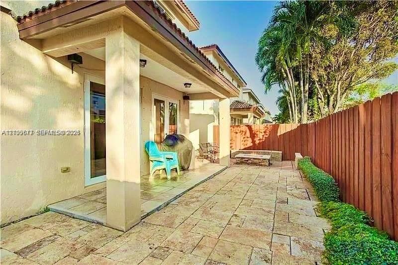 Covered patio featuring stone-tiled flooring, built-in masonry fire pit, and privacy wood fencing