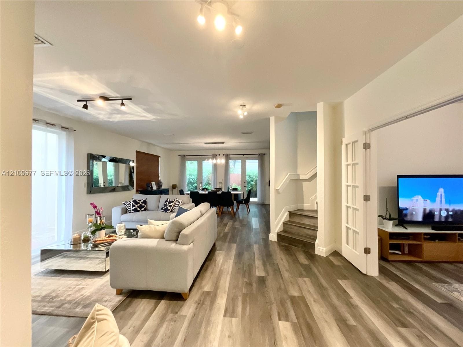 Open floor plan featuring wood-finish flooring, recessed track lighting, double-door entry with glass panes, and stairs with wood-finish treads