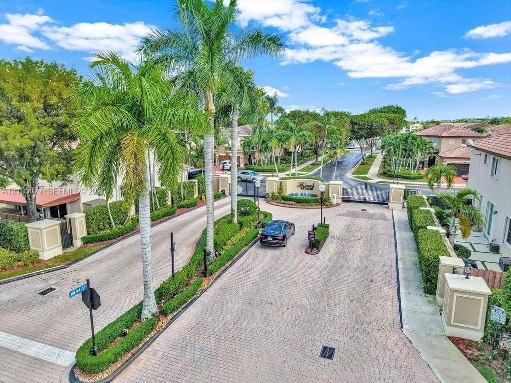 Gated community entrance featuring paver-stone driveways, ornamental stone pillars, professional landscaping with mature palm trees, and structural security gate