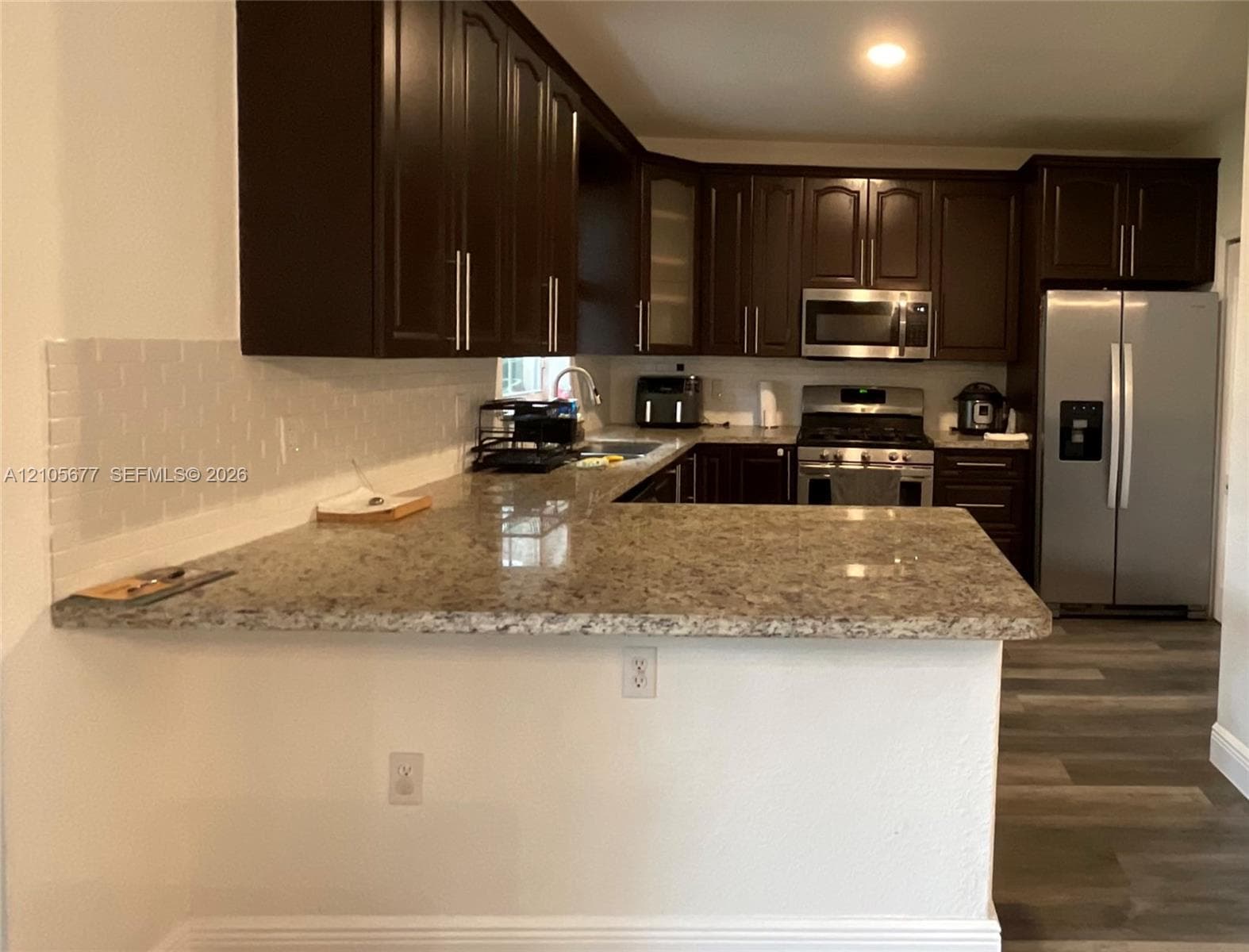 Kitchen featuring dark wood-finish cabinetry, stone-style countertops, white subway tile backsplash, stainless steel appliances, and wood-finish flooring