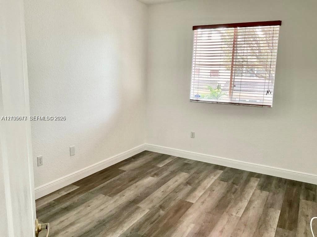 Neutral-toned interior room featuring wood-finish flooring, white walls, and a window with horizontal blinds