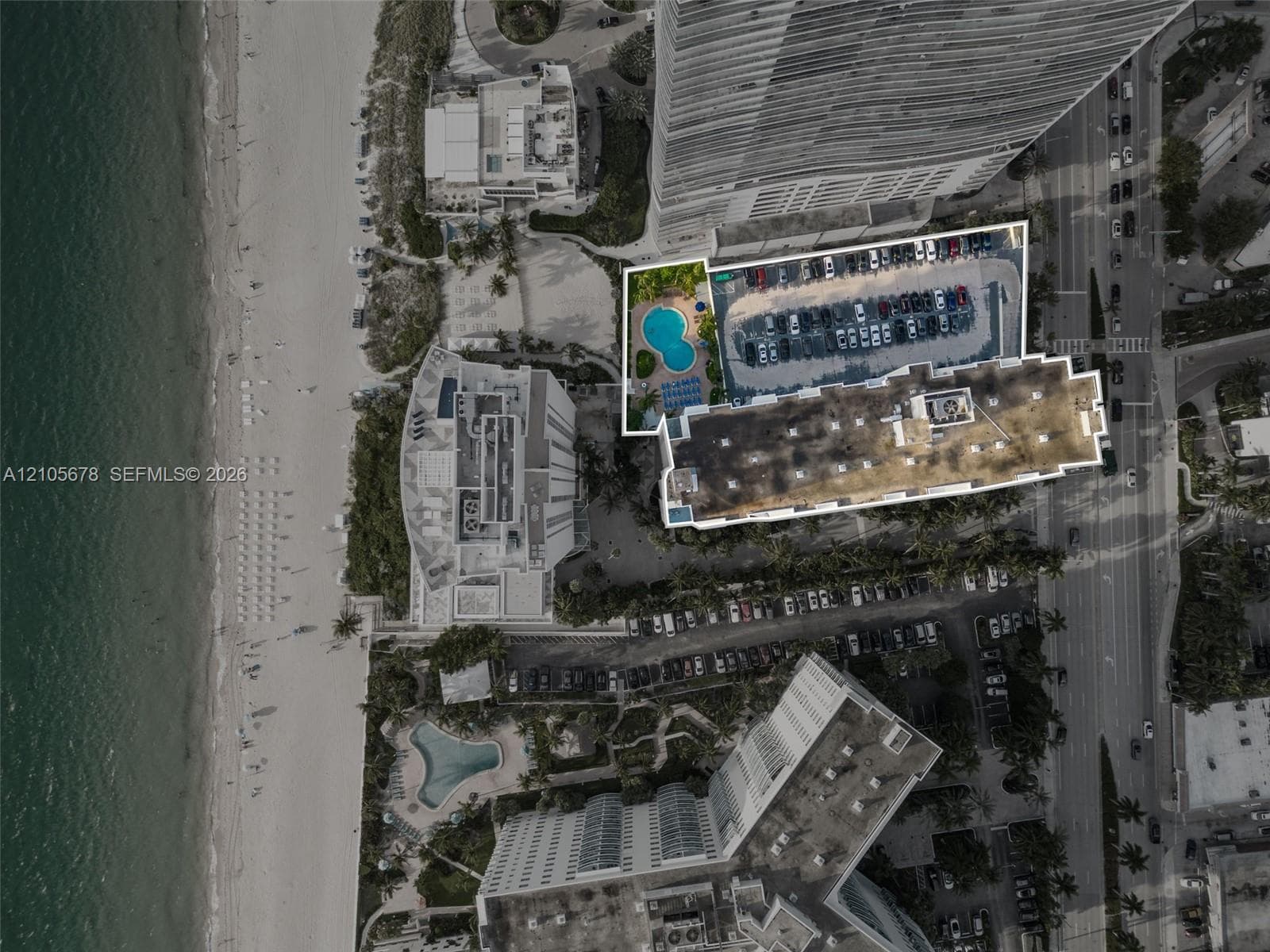 Aerial perspective of oceanfront property featuring a dedicated swimming pool, surface parking area, and direct proximity to the shoreline