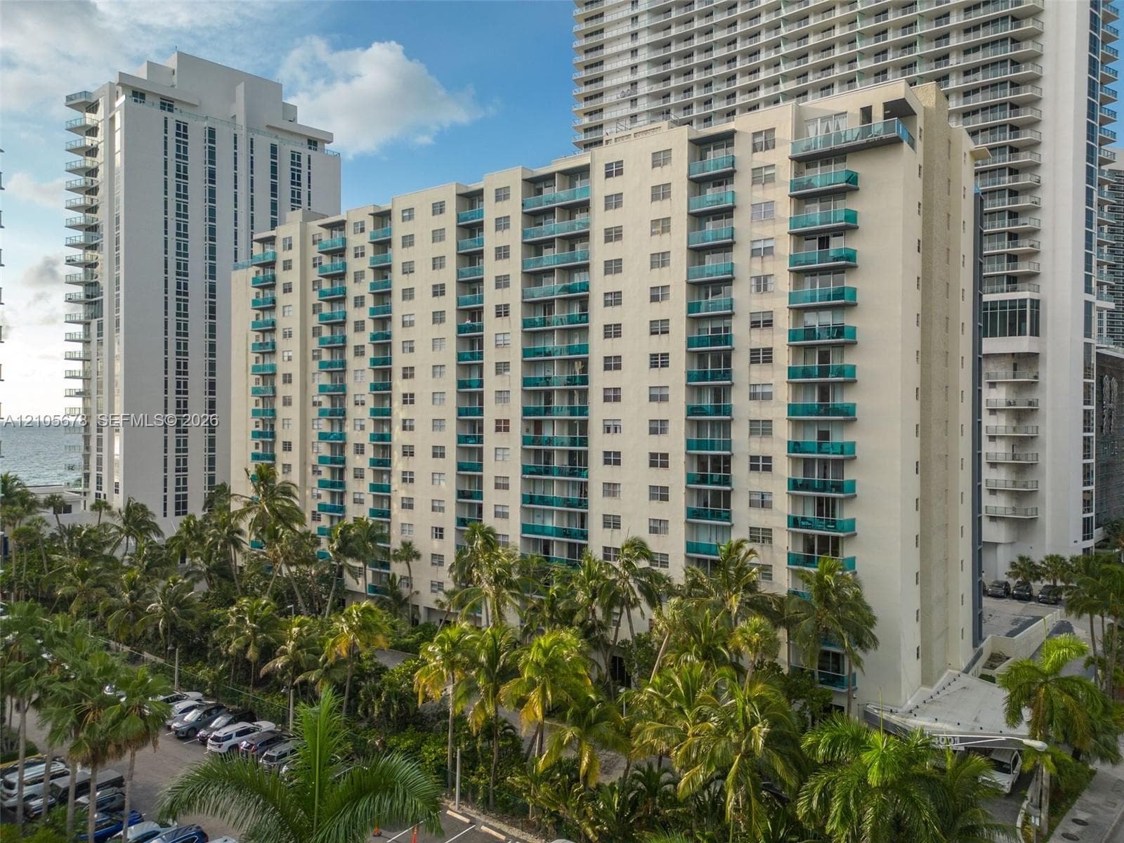 High-rise residential building featuring stacked balconies with glass railings and mature tropical landscaping