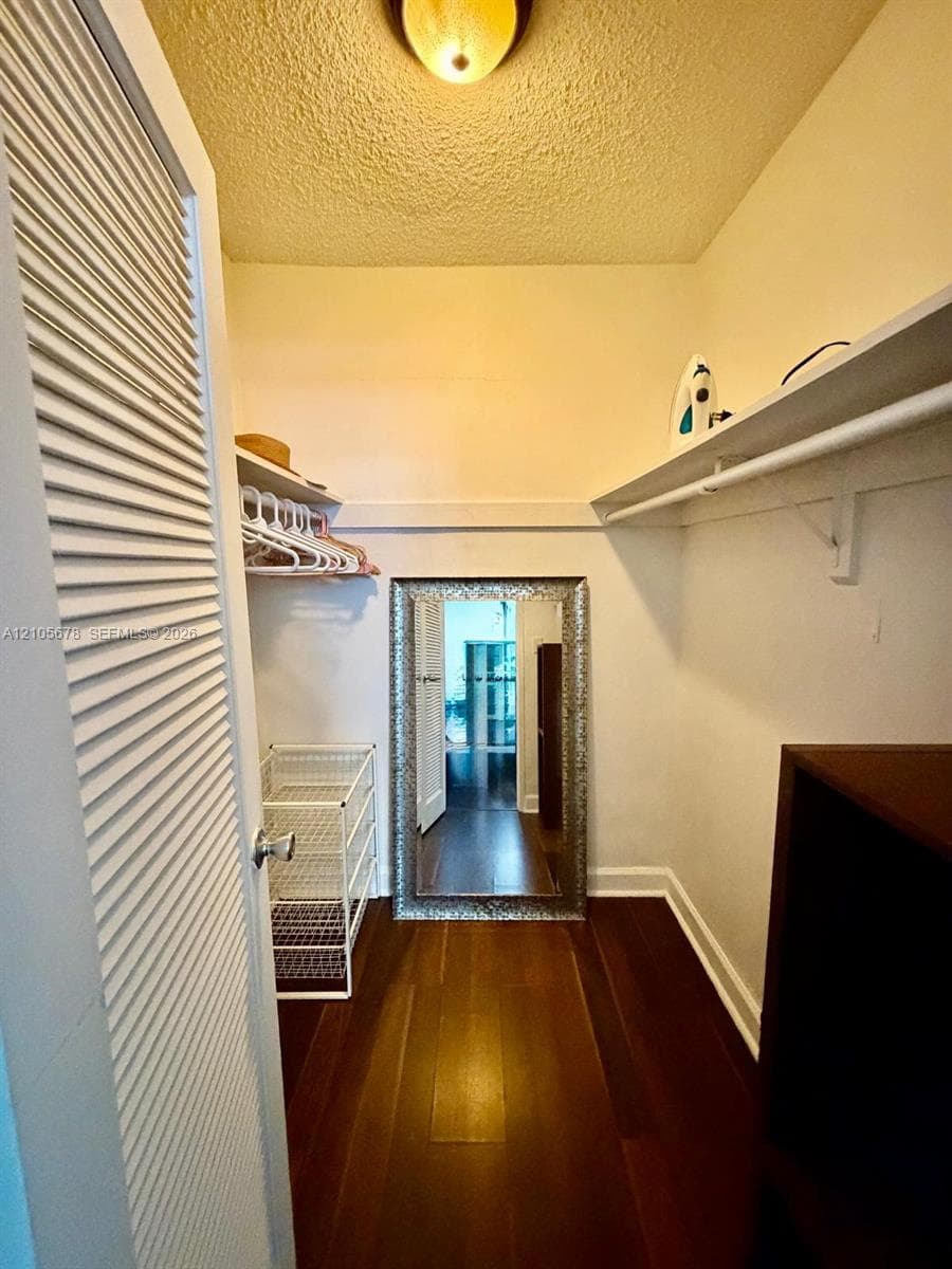 Storage space featuring louvered bi-fold doors, wood-finish flooring, and built-in upper shelving with integrated hanging rods