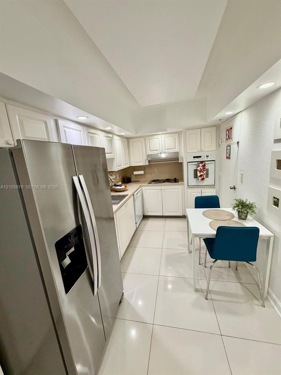 Kitchen featuring white cabinetry, stainless steel side-by-side refrigerator, built-in wall oven, recessed lighting, and large-format tile flooring