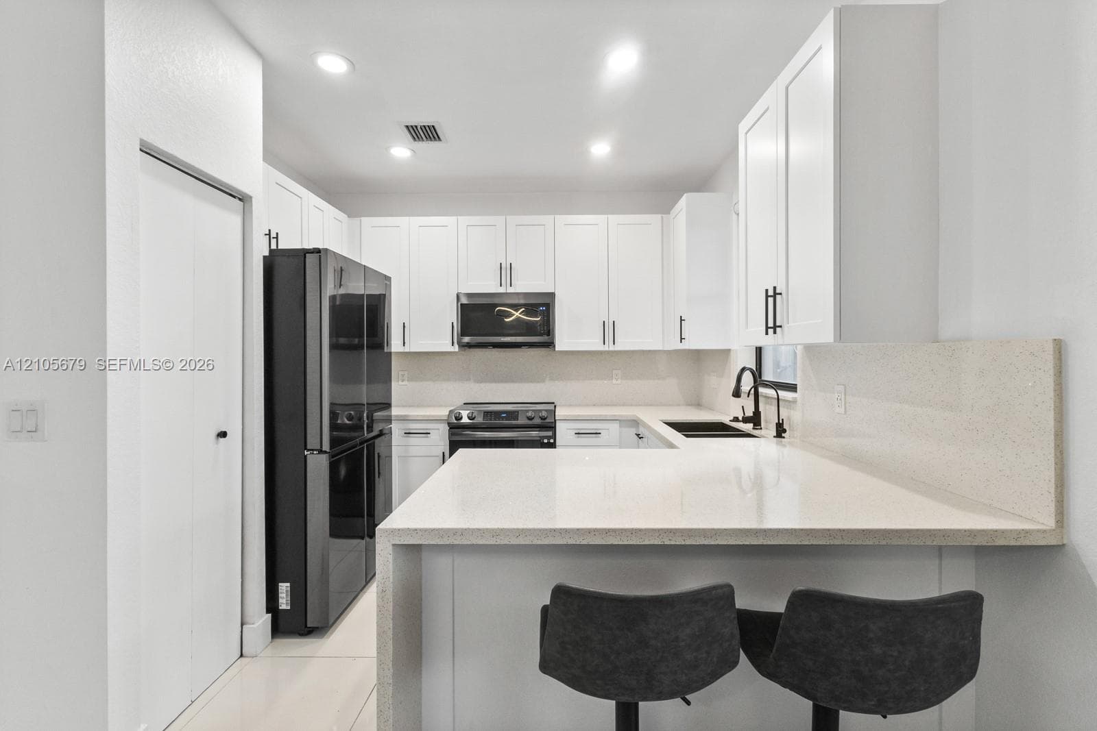 Kitchen featuring white Shaker-style cabinetry, quartz countertops, a stone-surfaced backsplash, black hardware, and recessed lighting