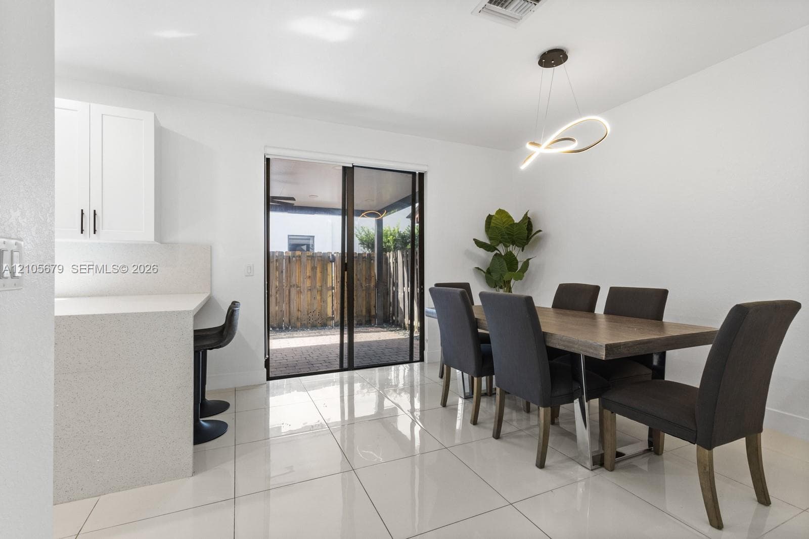 Polished porcelain flooring, quartz breakfast bar, white cabinetry, architectural LED pendant lighting, and sliding glass patio doors
