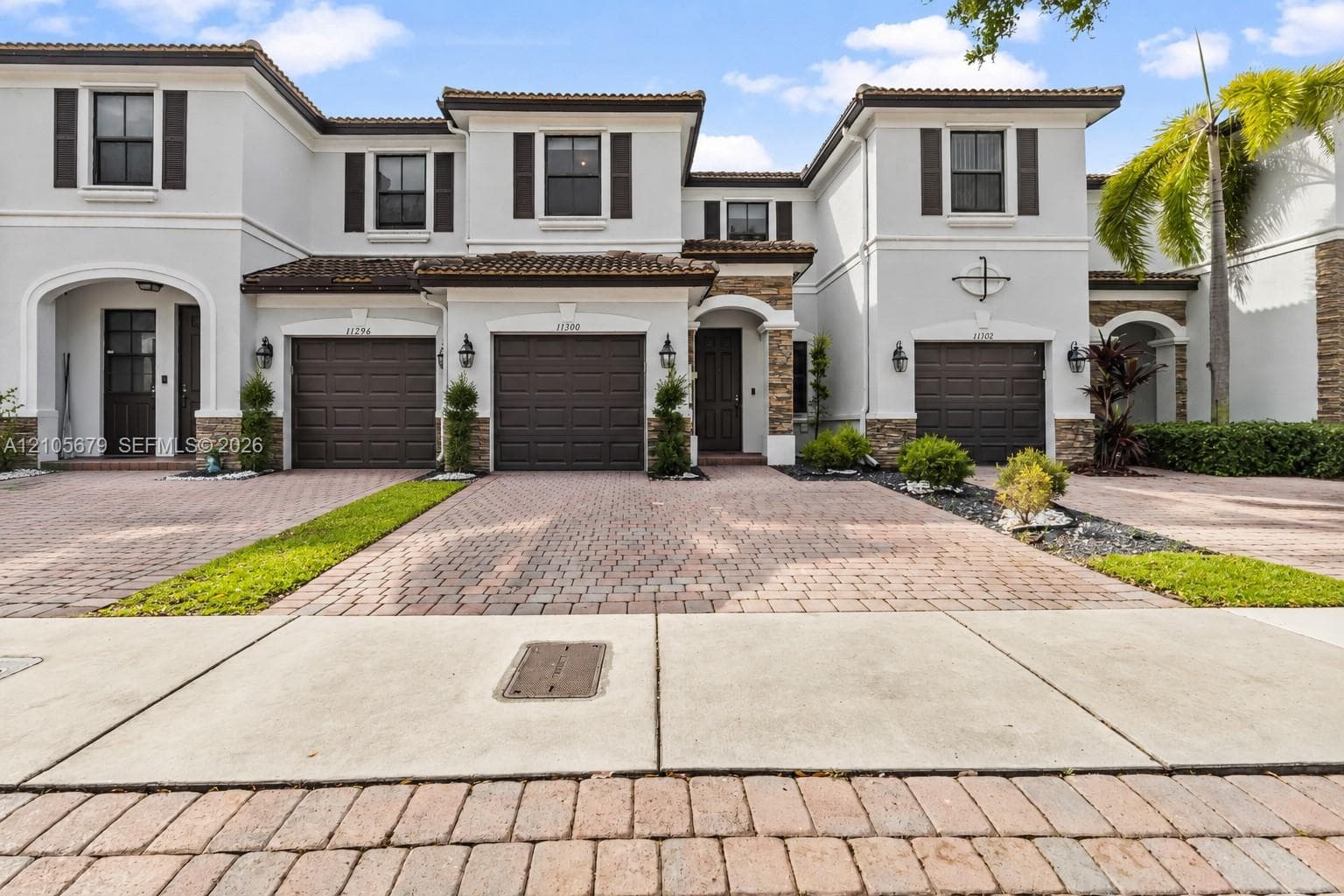 Mediterranean-inspired townhome exterior featuring multi-toned stone masonry accents, paver driveways, decorative shutters, and tile roofing