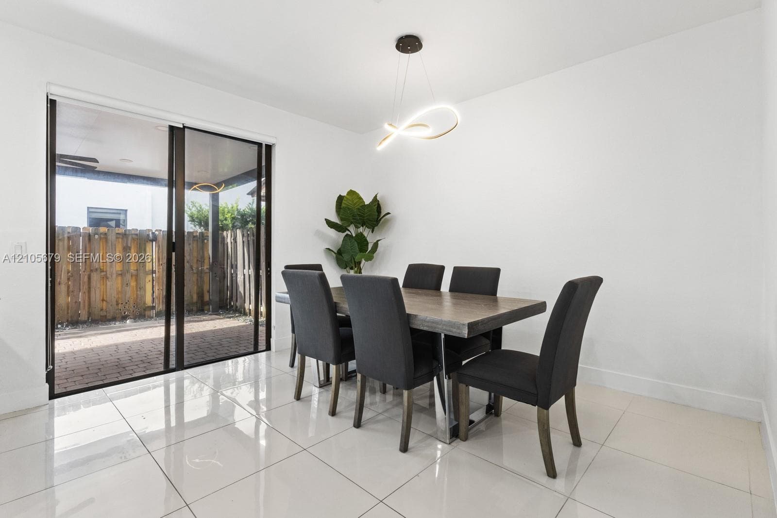 Large-format neutral tile flooring, modern sculptural pendant lighting, and oversized sliding glass doors leading to a paved patio area