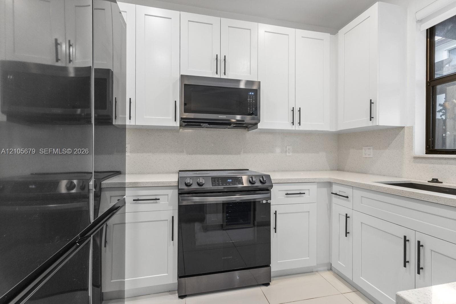 Kitchen featuring white shaker-style cabinetry, solid-surface countertops, stone-finish backsplash, and stainless steel appliances including a built-in microwave and range