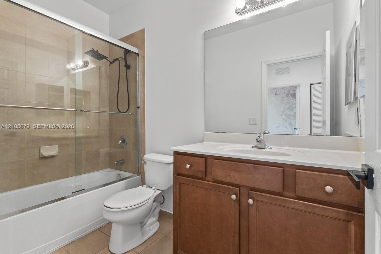 Bathroom featuring a wood-finish vanity with a white countertop, large frameless mirror, glass-enclosed shower with tiled surround, and a rainfall showerhead