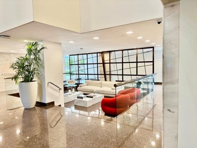 Polished stone flooring, recessed ceiling lighting, decorative grid-pattern metal room divider, and glass panel railing with a stainless steel handrail