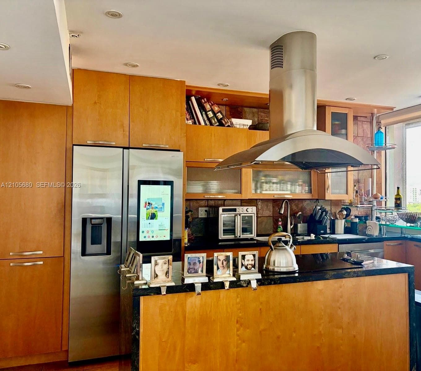 Kitchen featuring custom wood cabinetry, stainless steel appliances, a large center island with a dark stone countertop, and a stainless steel wall-mounted range hood