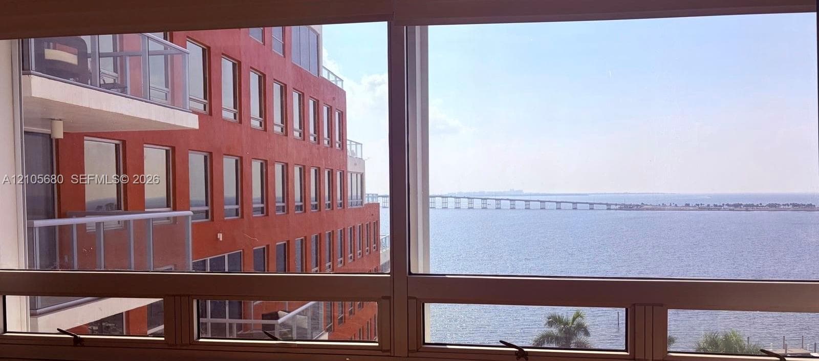 Large multi-pane window with metal frames, expansive water horizon, and bridge backdrop