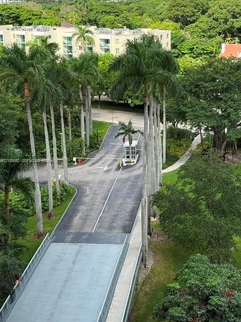 Gated entrance featuring a security guard booth, paved driveway, mature palm trees, and manicured landscaping