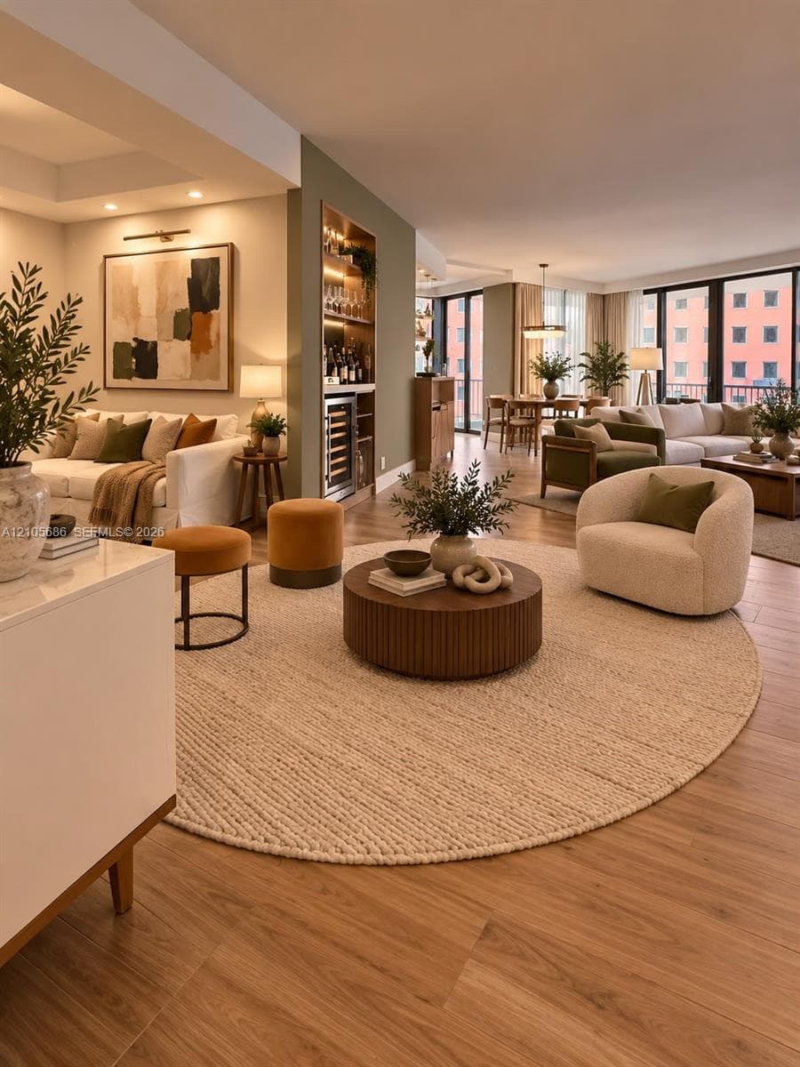 Open-concept interior featuring wood-finish flooring, built-in recessed shelving with integrated lighting, a beverage refrigerator, and expansive floor-to-ceiling windows