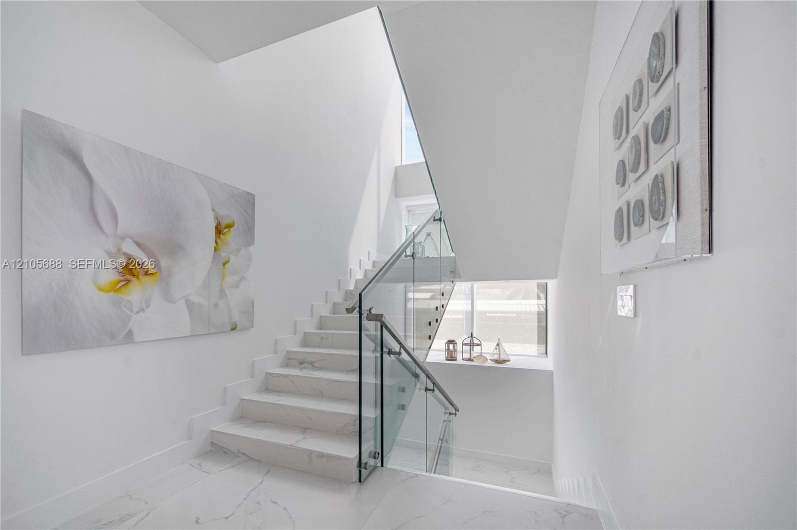 Staircase featuring white stone-finish steps, glass balustrade, metal handrails, and a multi-level window design