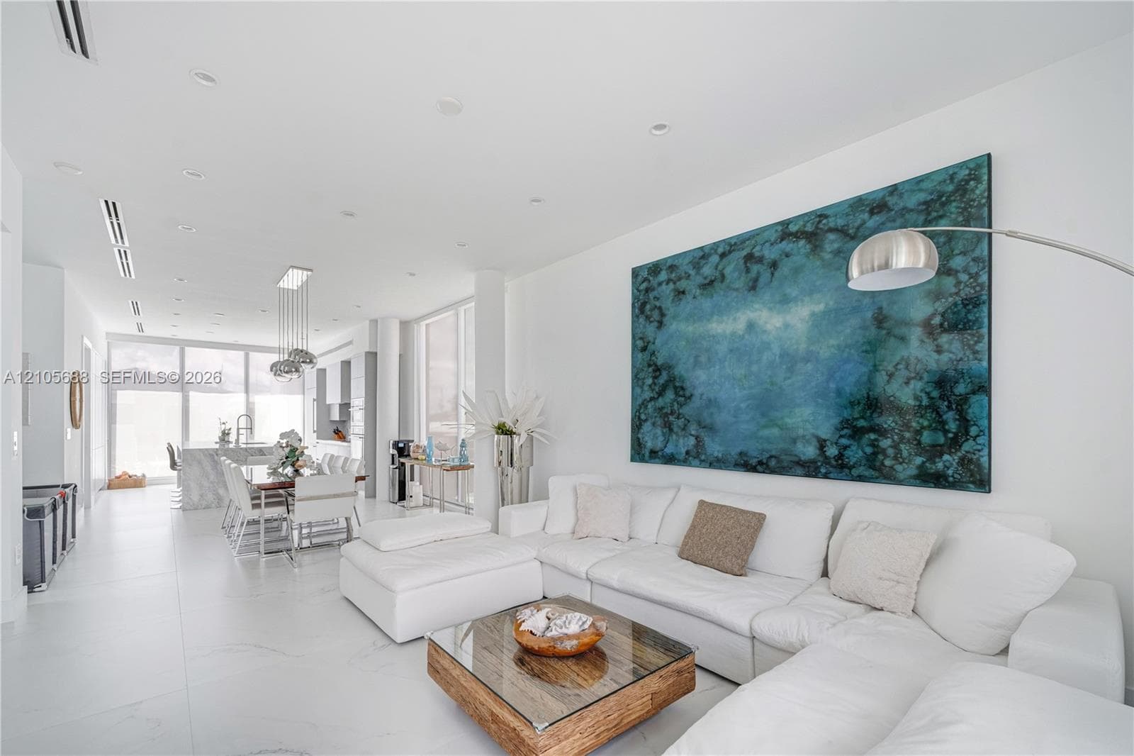 Open-concept interior featuring large-format porcelain tile flooring, recessed ceiling lighting, floor-to-ceiling windows, and a central kitchen island with a stone-finish countertop