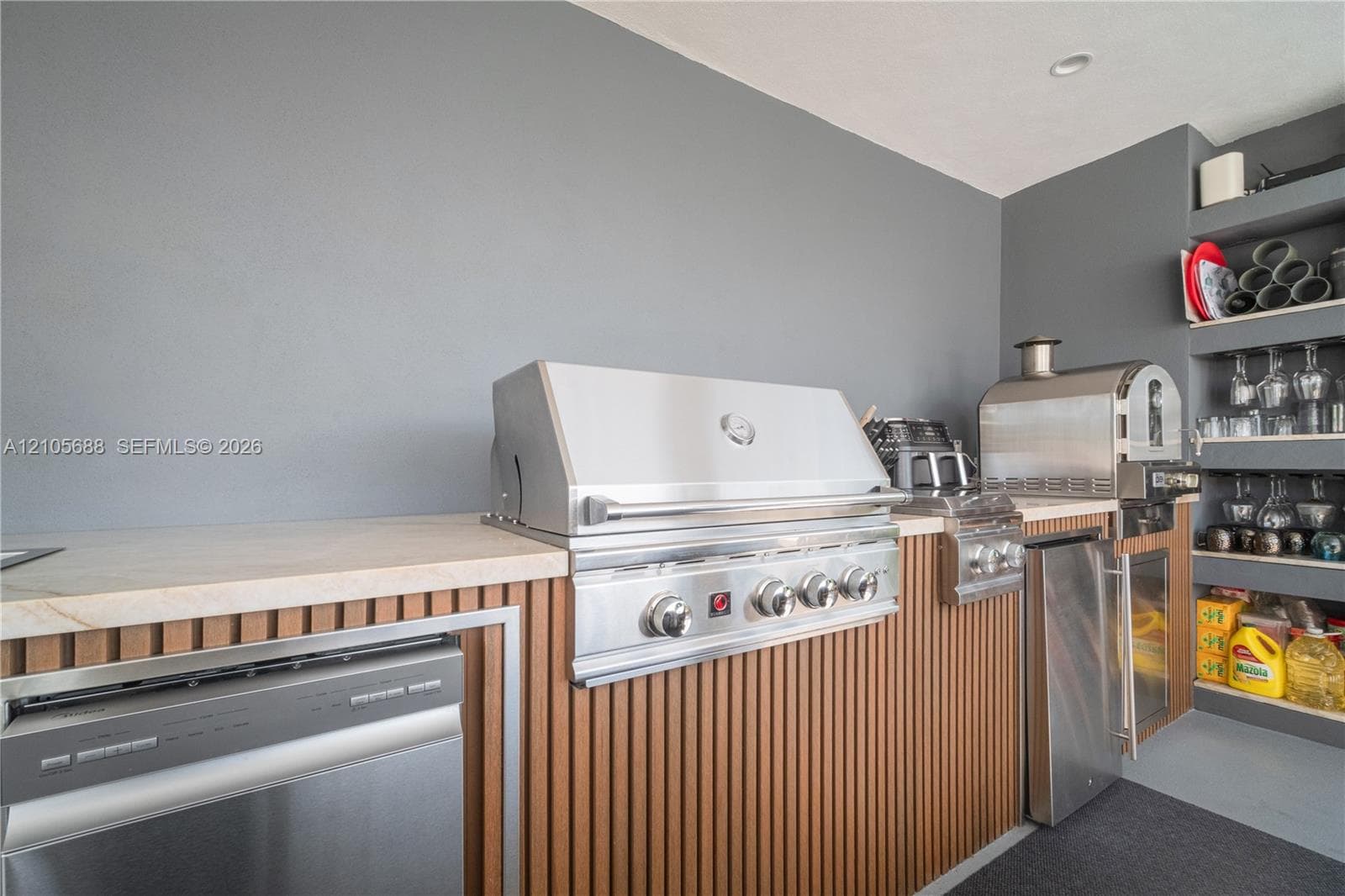 Outdoor kitchen featuring stainless steel appliances, stone-look countertops, vertical wood-slat cabinetry, and integrated shelving