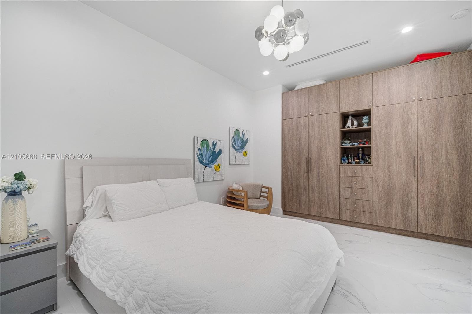 Full-height built-in wood-finish cabinetry featuring integrated open shelving and drawers, polished white stone-finish flooring, and a modern multi-globe chandelier