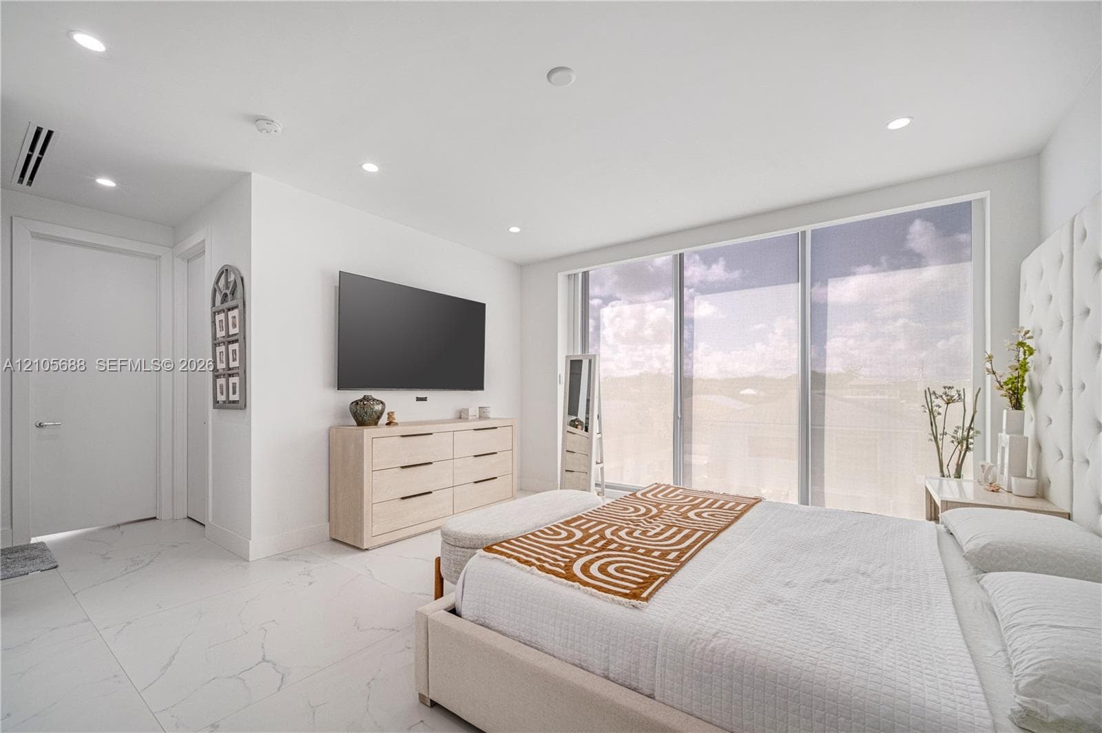 Floor-to-ceiling glass sliding doors, recessed lighting, white stone-finish flooring, and a floor-to-ceiling tufted wall panel