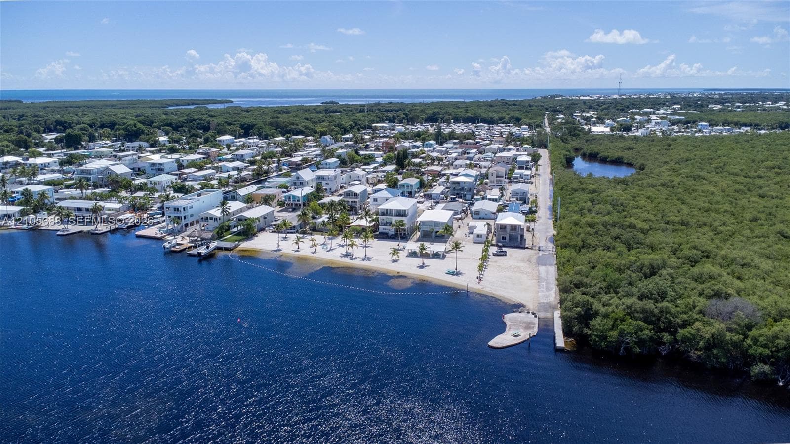 Community Beach and Ramp Aerial perspective featuring direct waterfront access, a private sandy shoreline, palm tree landscaping, and a concrete boat ramp