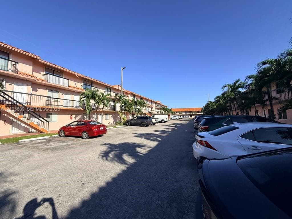 Multi-story residential complex featuring stucco exterior walls, terracotta-style roofing, metal balcony railings, and surface-level asphalt parking