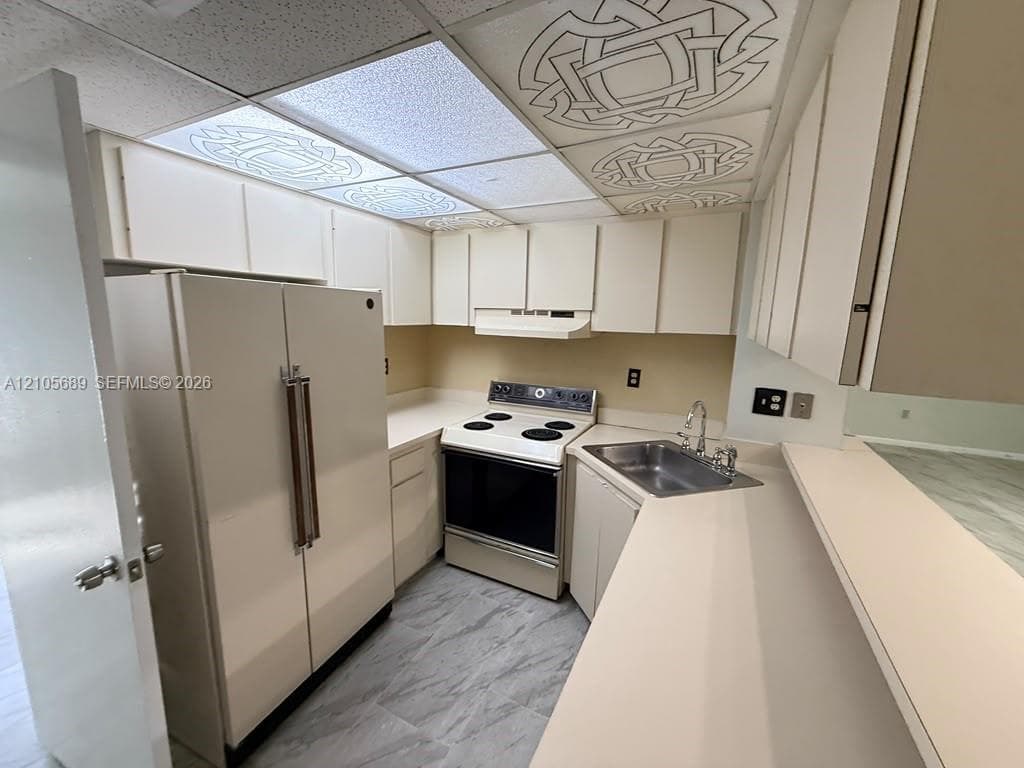 Galley kitchen featuring stainless steel appliances, white cabinetry, laminate countertops, and tile flooring