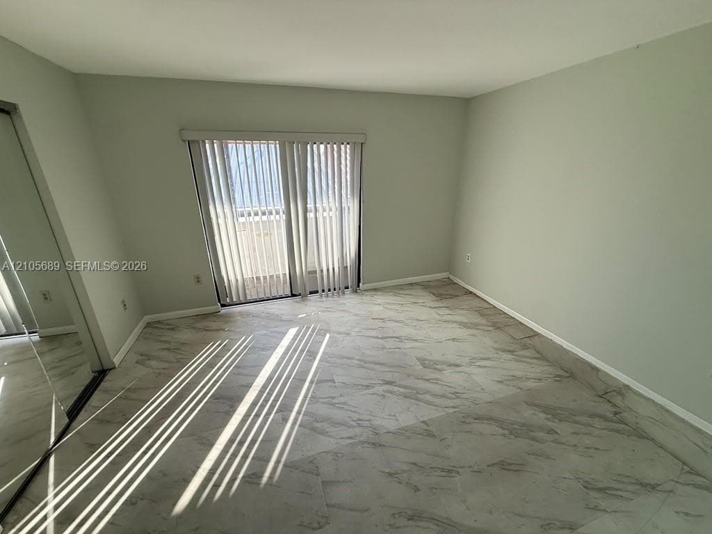 Neutral-toned room featuring large-format stone-patterned tile flooring, floor-to-ceiling mirrored closet doors, and a sliding glass door with vertical blinds
