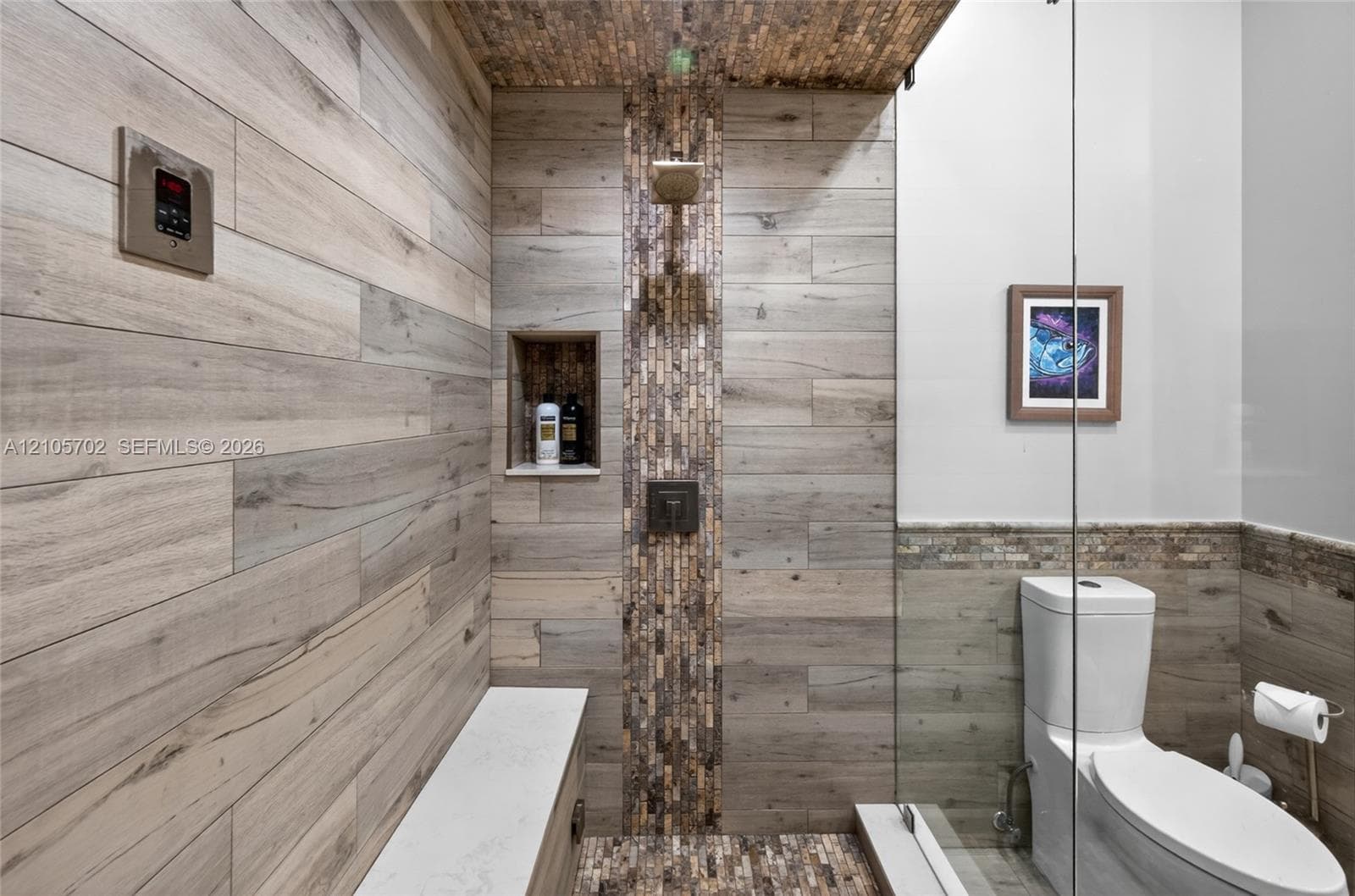 Walk-in shower featuring wood-finish tile walls, a vertical mosaic tile inlay, a built-in recessed shelf, a rain showerhead, and a frameless glass enclosure