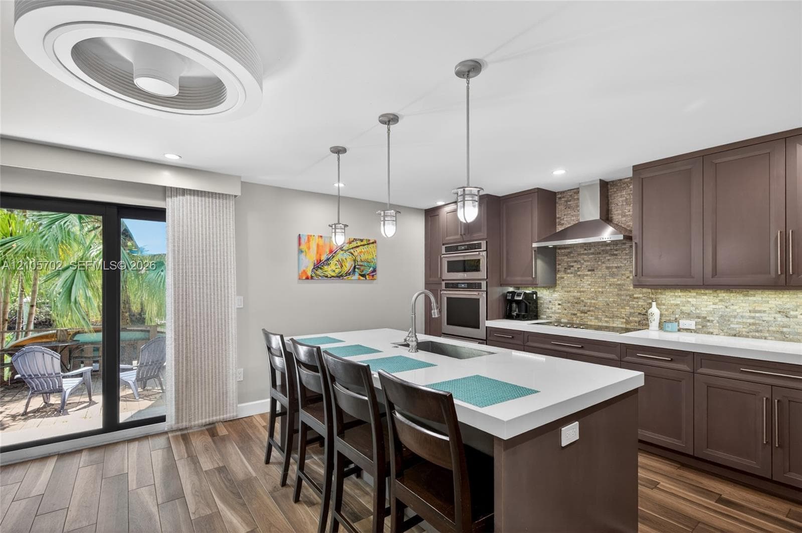 Kitchen featuring a central island with a quartz countertop, dark cabinetry, stone-veneer backsplash, stainless steel wall-mounted oven, and a ceiling-mounted orbital fan