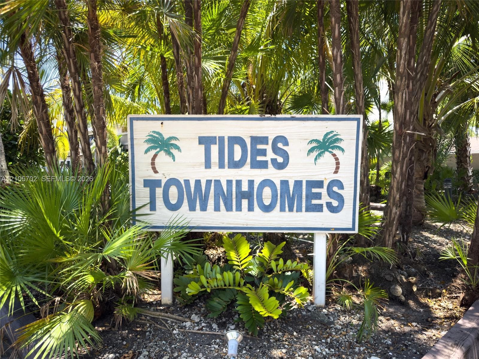 Freestanding community signage surrounded by mature palm trees and established tropical landscaping