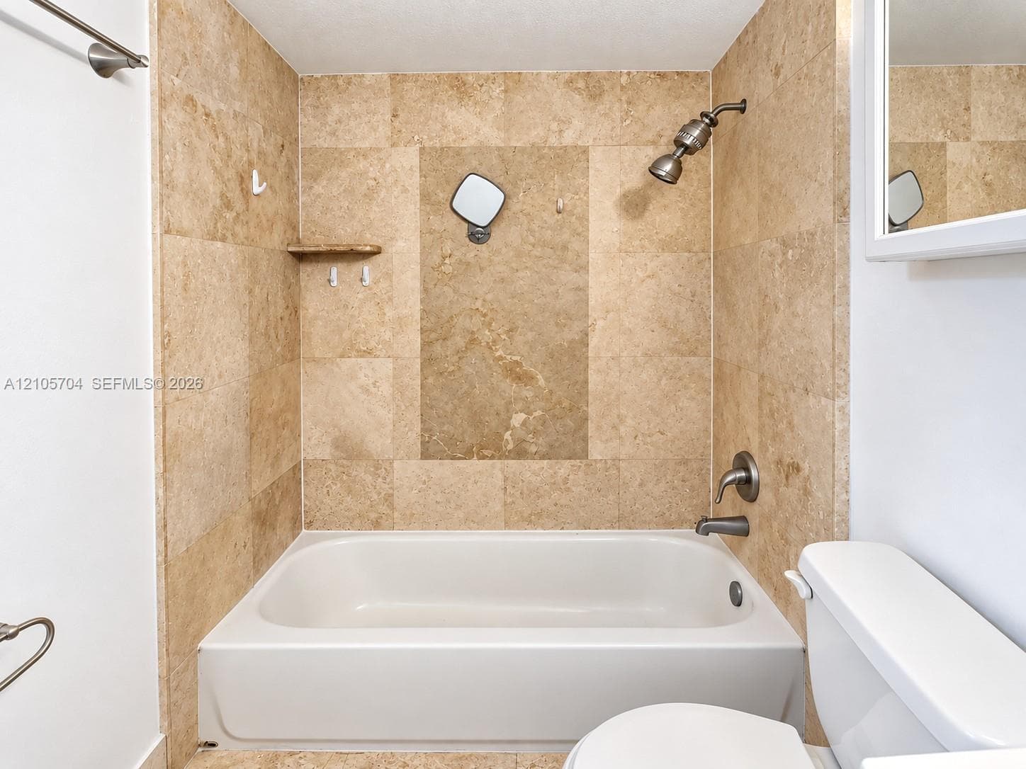 Full-height natural stone tile surround, integrated built-in corner shelf, white porcelain bathtub, and metallic shower hardware