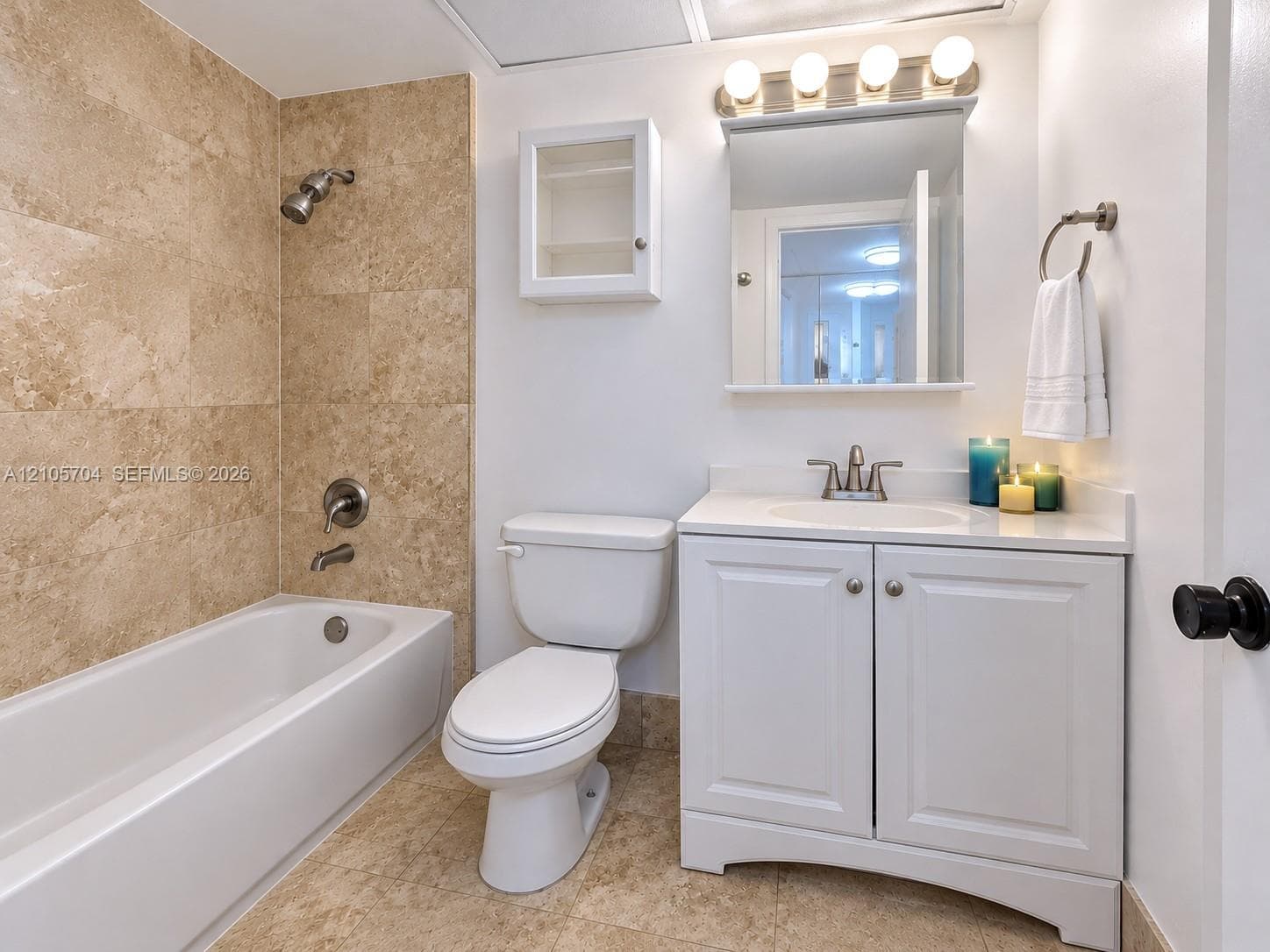 Bathroom featuring stone-tile tub surround, white vanity with integrated sink, wall-mounted medicine cabinet, and four-light vanity fixture